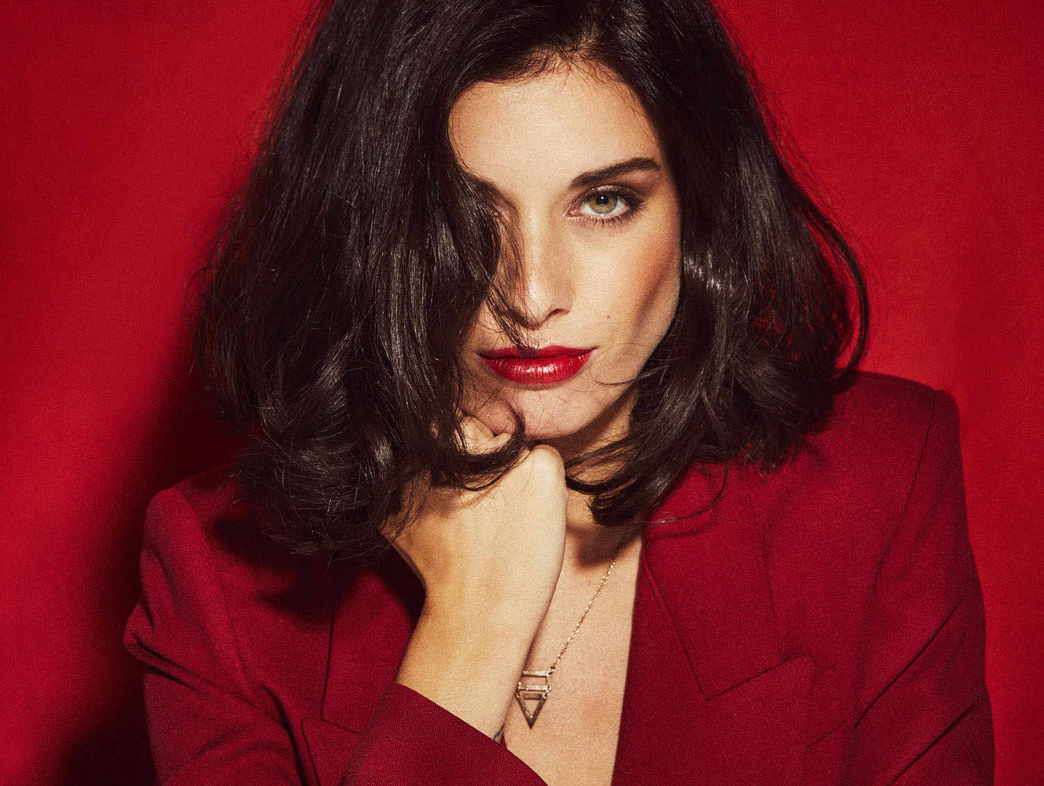 Plano entero con pose geométrica y sombra dura en fondo rojo